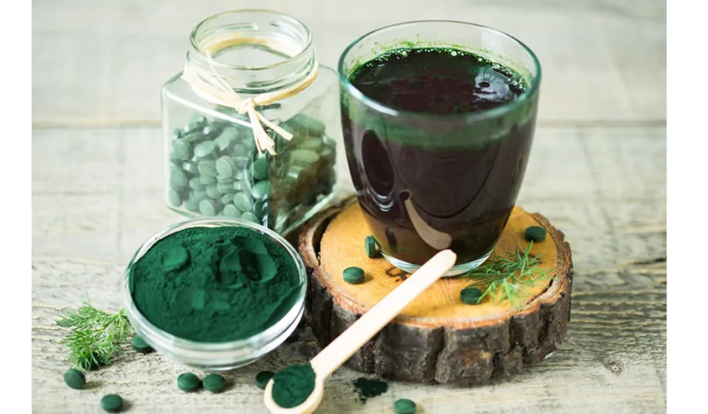 Espirulina para deportistas | Vaso de jugo de espirulina sobre una mesa de madera, acompañado de polvo y tabletas de espirulina, promoviendo la salud y la energía de los deportistas.